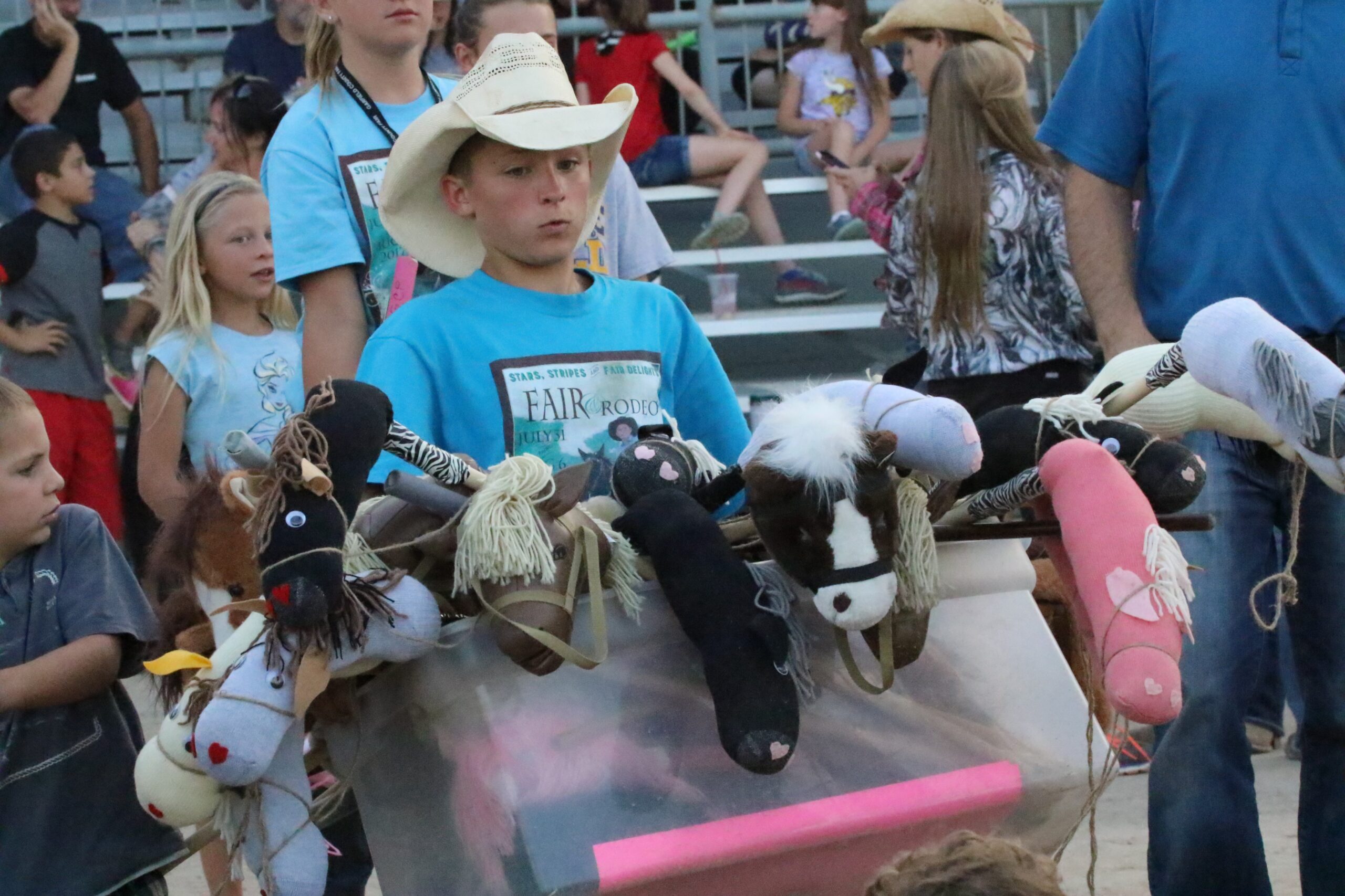 A young volunteer in a cowboy hat carries stick horses at the Garfield County Fair and Rodeo in Rifle, CO. 